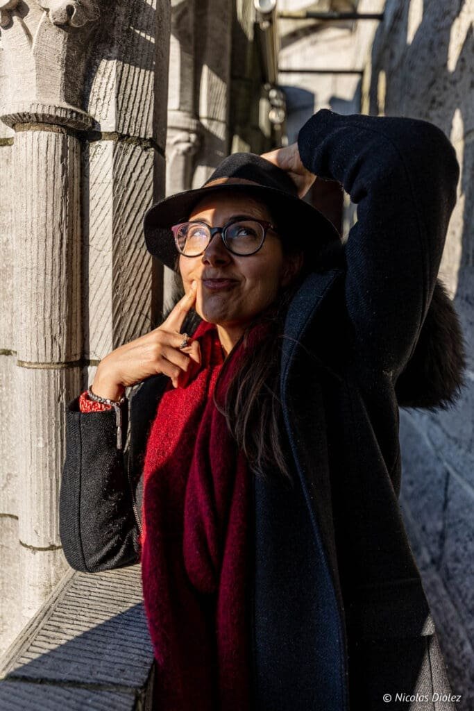 Turiste souriante avec chapeau et écharpe rouge près d'une colonne du Beffroi de Gand.