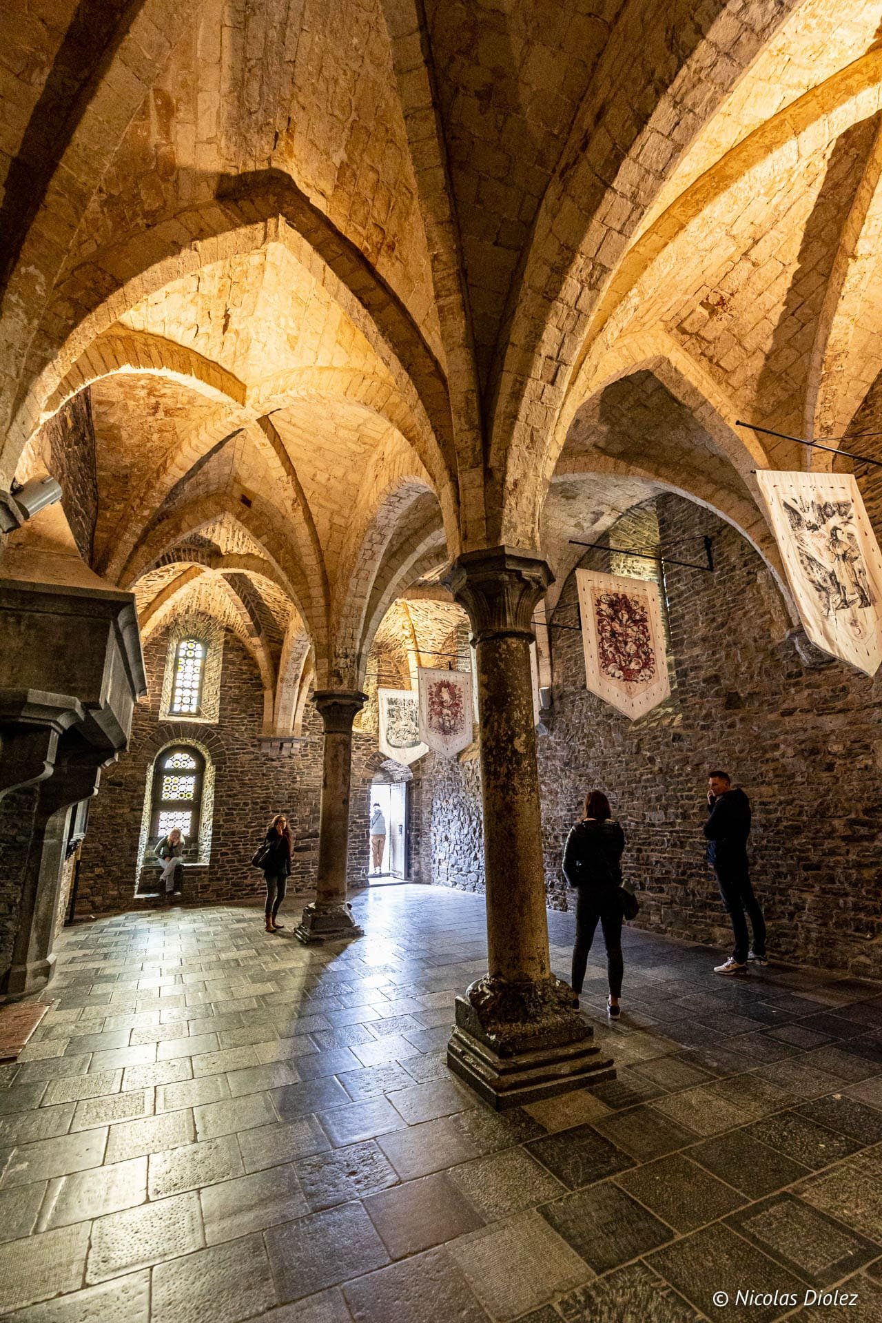 Intérieur voûté en pierre du Château des Comtes à Gand avec visiteurs et bannières.