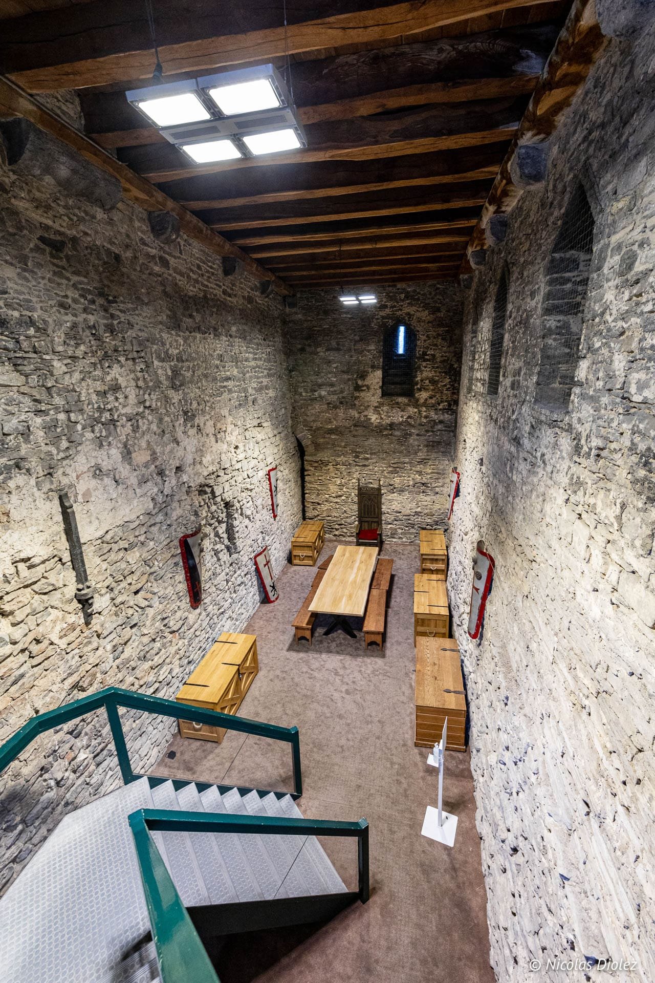 Intérieur médiéval du Château des Comtes de Gand avec escalier, table et coffres en bois.