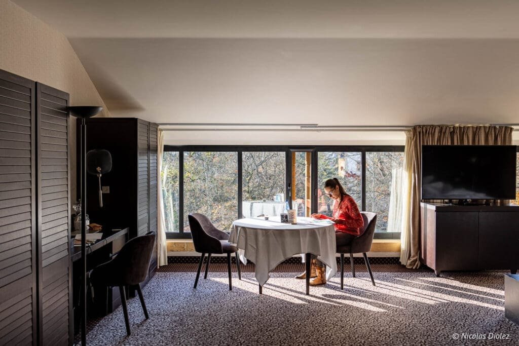 Chambre d'hôtel MGallery La Citadelle Metz avec femme lisant près d'une fenêtre.
