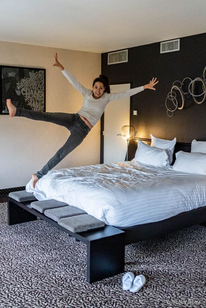 Femme sautant sur le lit dans une chambre d'hôtel MGallery La Citadelle Metz.