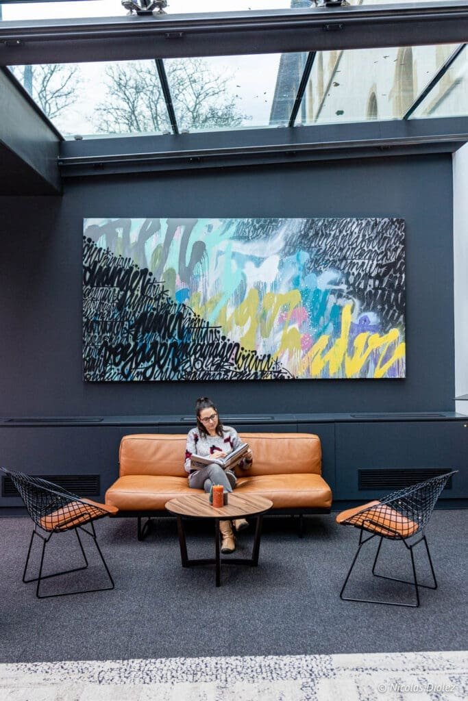 Lobby Hôtel MGallery La Citadelle Metz avec femme lisant sur canapé cuir.
