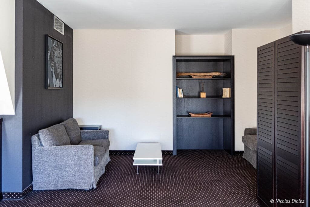 Salon de l'Hôtel MGallery La Citadelle Metz avec canapé gris et étagère noire.