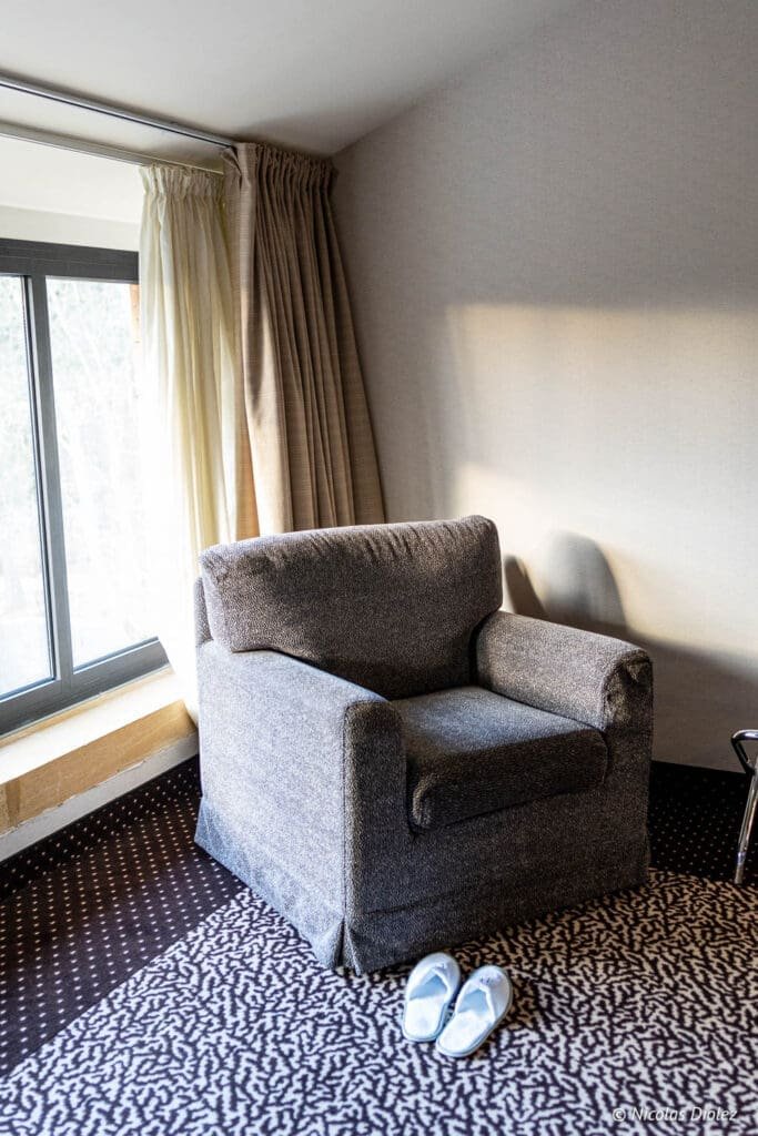Fauteuil et chaussons dans une chambre de l'Hôtel MGallery La Citadelle Metz.