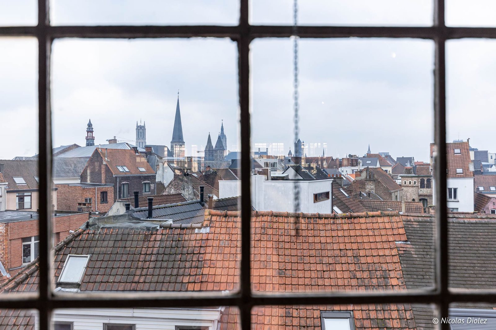Vue sur les toits de Gand et ses clochers à travers une fenêtre.