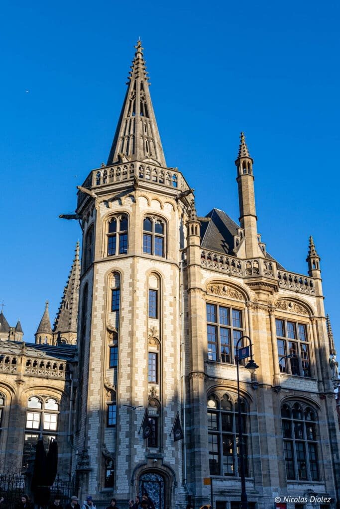Architecture gothique de Gand avec haute flèche sous un ciel bleu clair.