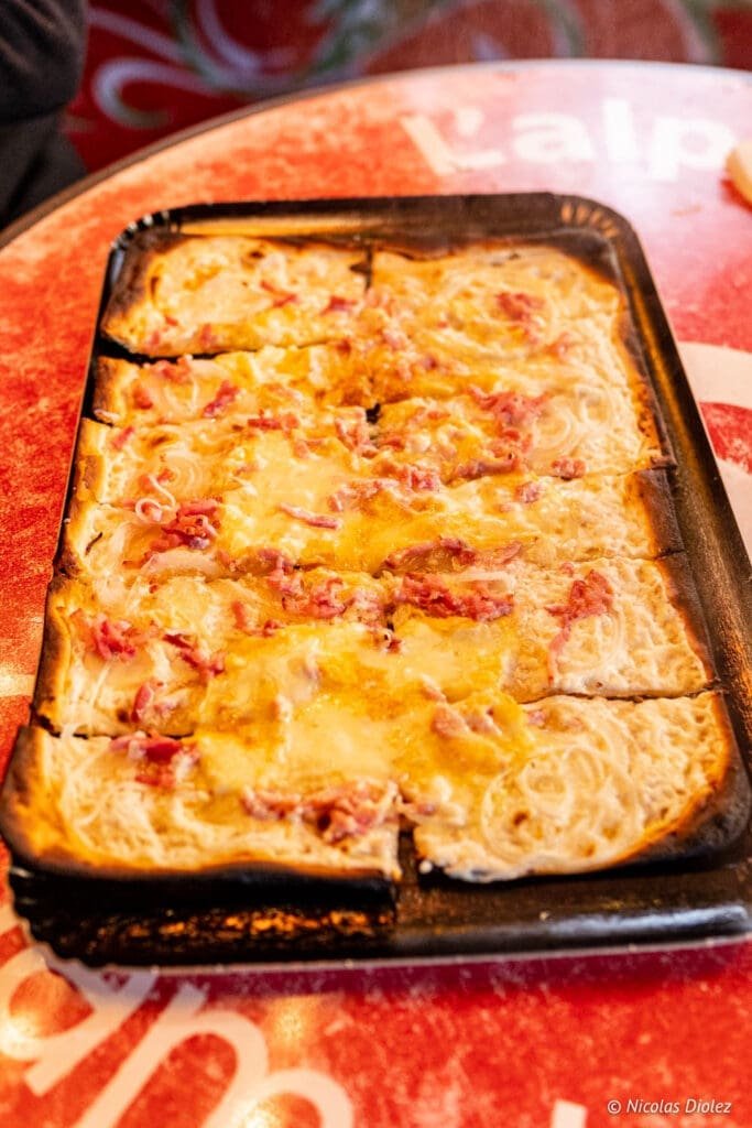 Tarte flambée traditionnelle coupée en parts sur un plateau rouge.