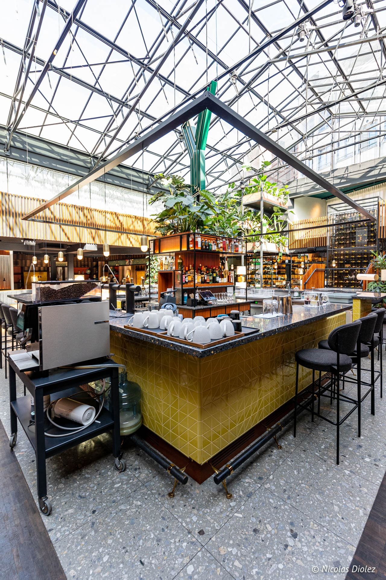 Bar du Yalo Hôtel Gand sous une verrière avec plantes et machine à café.