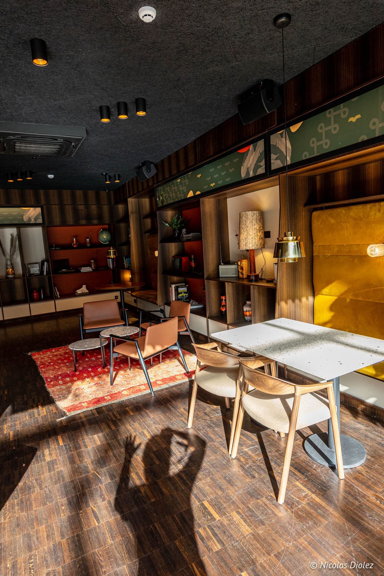 Intérieur du Yalo Hotel Gand: salon moderne avec sièges en cuir et bois, tapis rouge et ombre au sol.