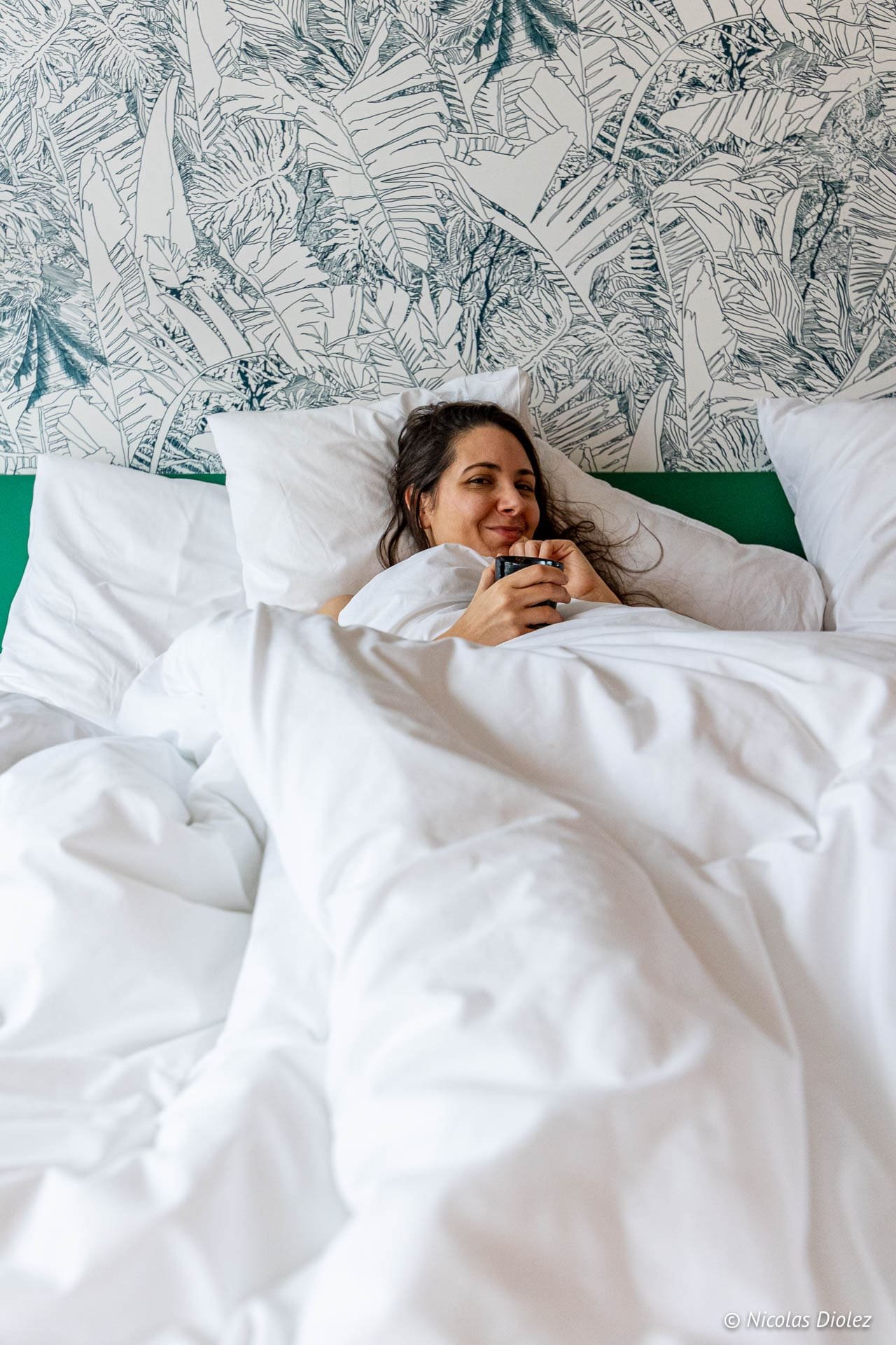 Femme souriante au lit dans une chambre d'hôtel Yalo à Gand.