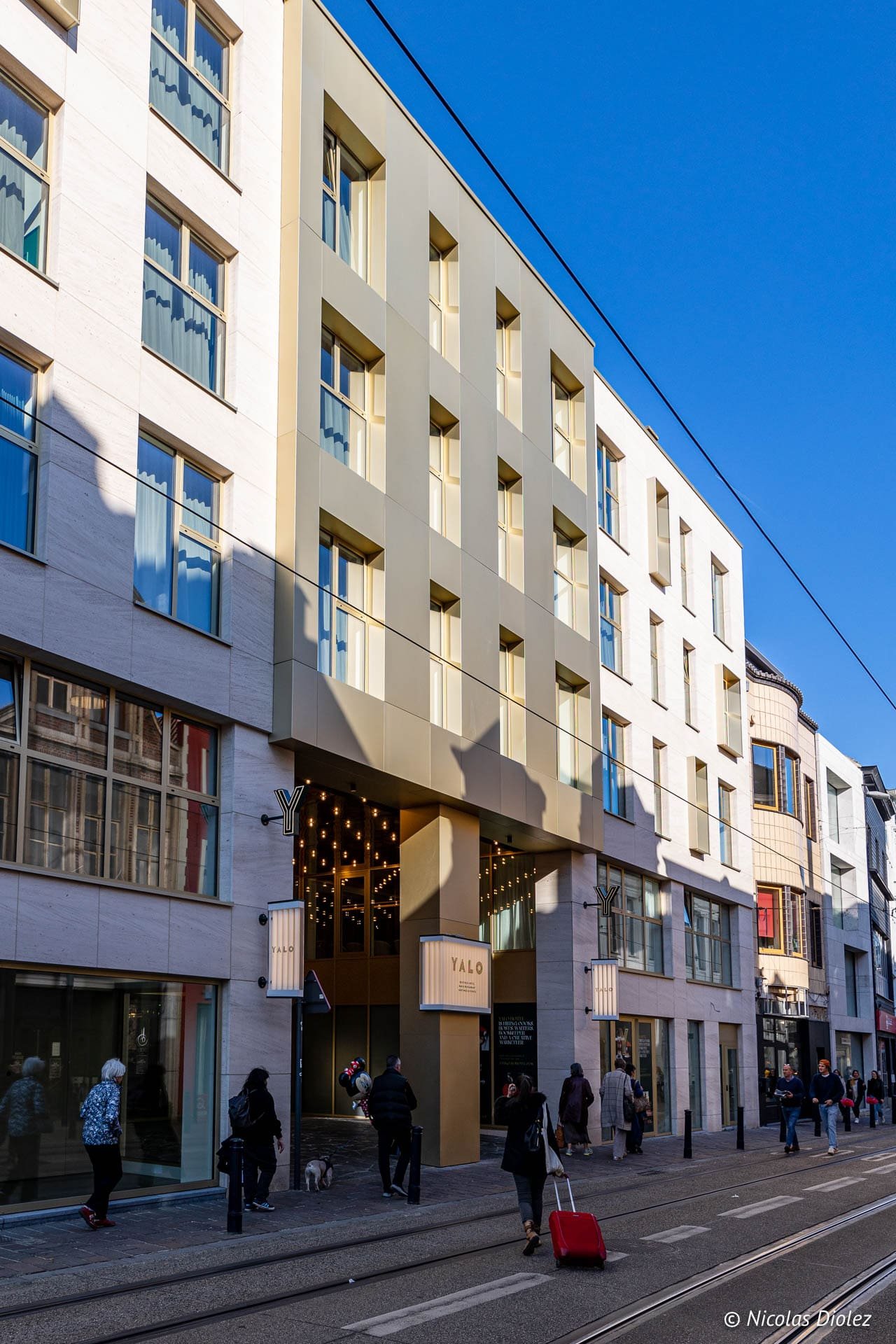 Hôtel Yalo Gand façade moderne avec tramway et piétons sur le trottoir.