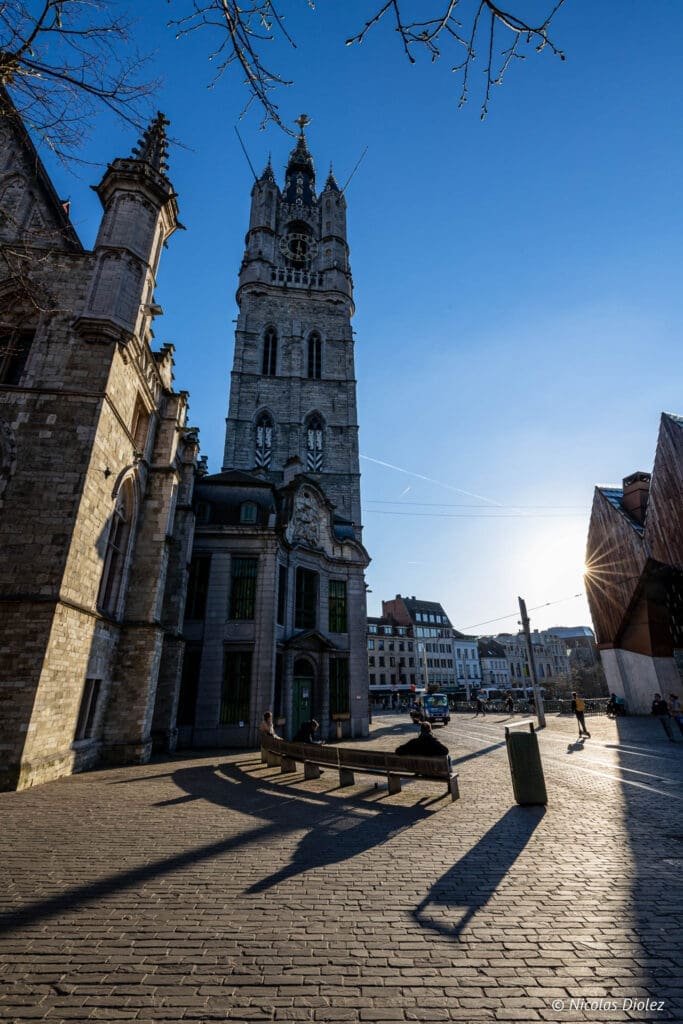 Beffroi de Gand et bâtiment adjacent sur une place pavée.
