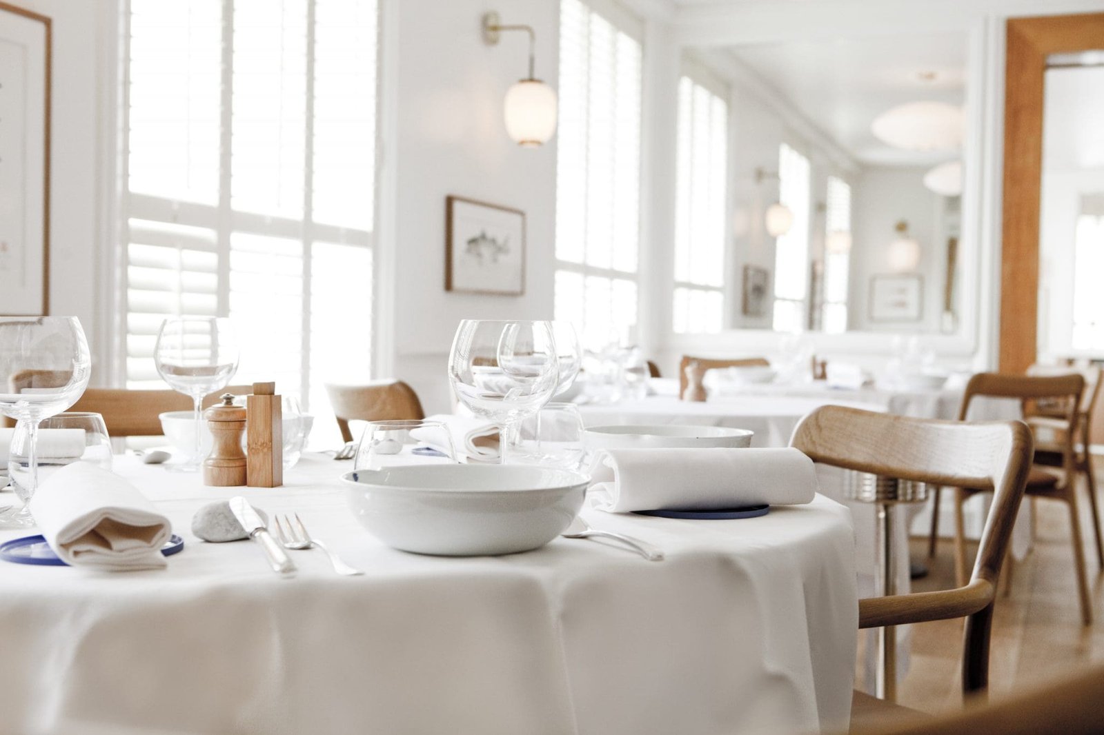 RECH salle-®pierremonetta Table dressée avec vaisselle blanche, verres à pied et moulin à poivre, restaurant lumineux.