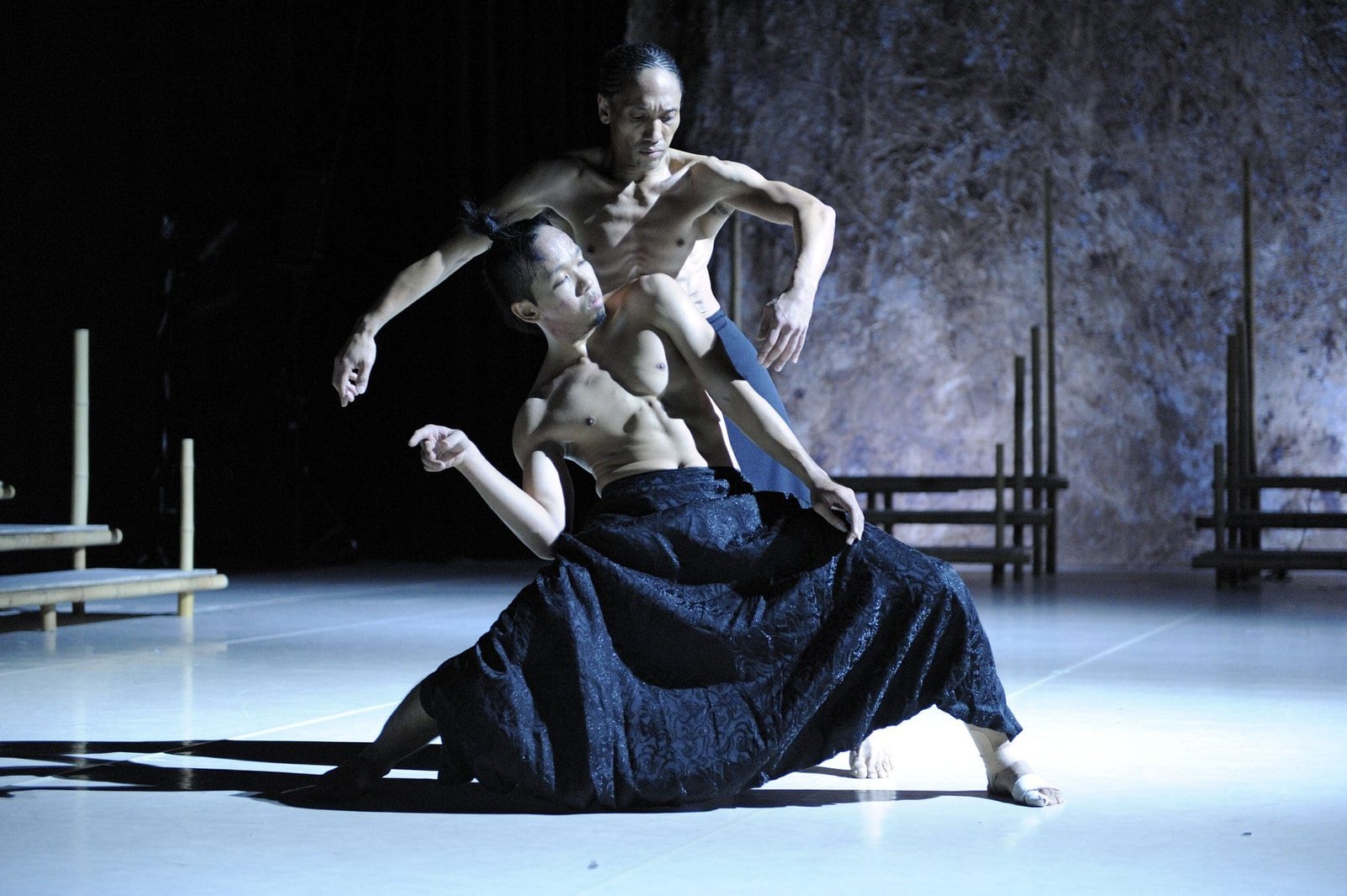 Danseurs contemporains hommes en mouvement sur scène sombre.