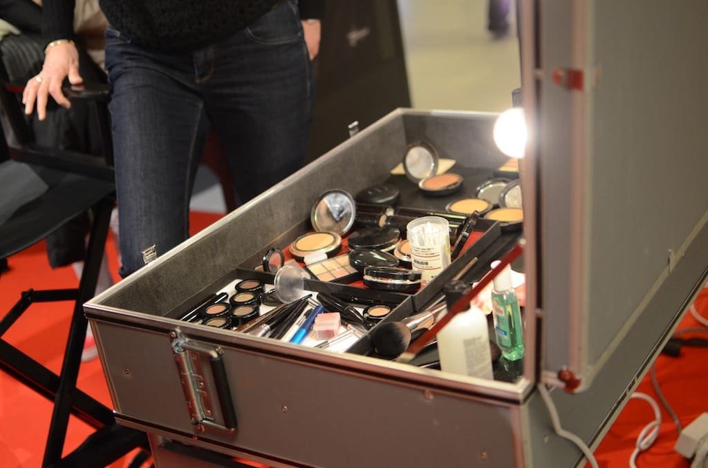 hartcourt_©Remi_BLOMME20 Valise de maquillage professionnelle ouverte, remplie de fards et pinceaux, près d'une personne.