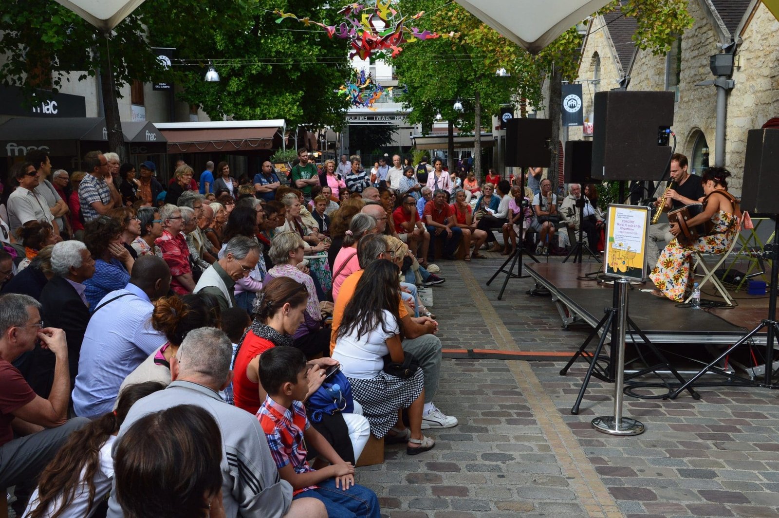 Concert de musique acoustique avec deux musiciens devant un public assis à Bercy Village.