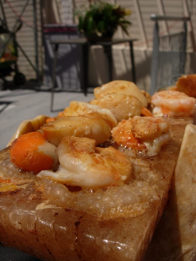 Crevettes et pétoncles grillés sur bloc de sel rose chauffé.