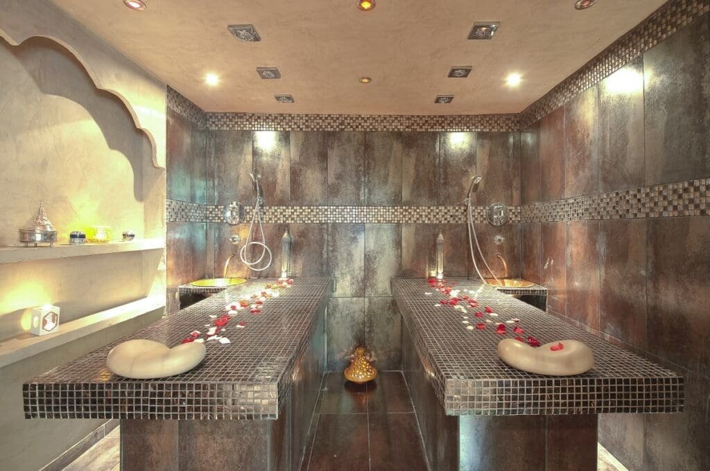 Salle de soins hammam double avec tables carrelées et pétales de rose.