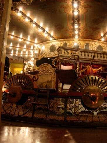 Manège ancien avec voiture décorée, éclairage festif et plafond peint.