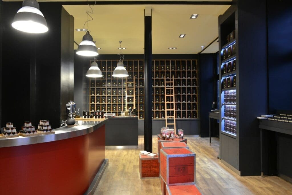 Intérieur boutique de thé à Paris avec comptoir rouge et étagères remplies de boîtes de thé.