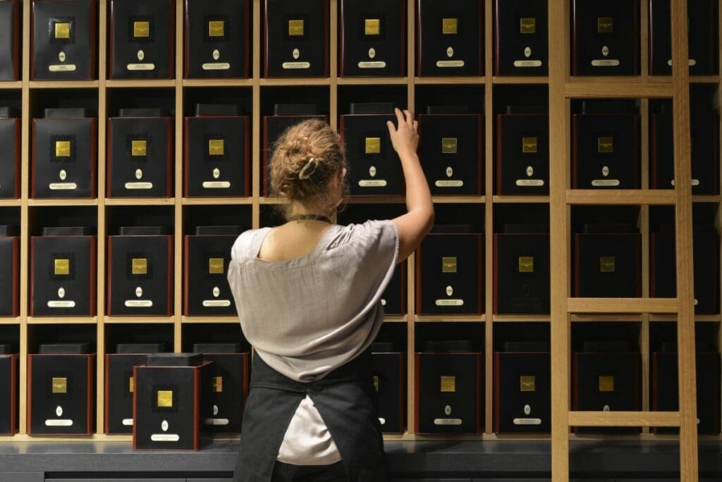 Employée choisissant une boîte de thé dans un mur d'étagères en bois.