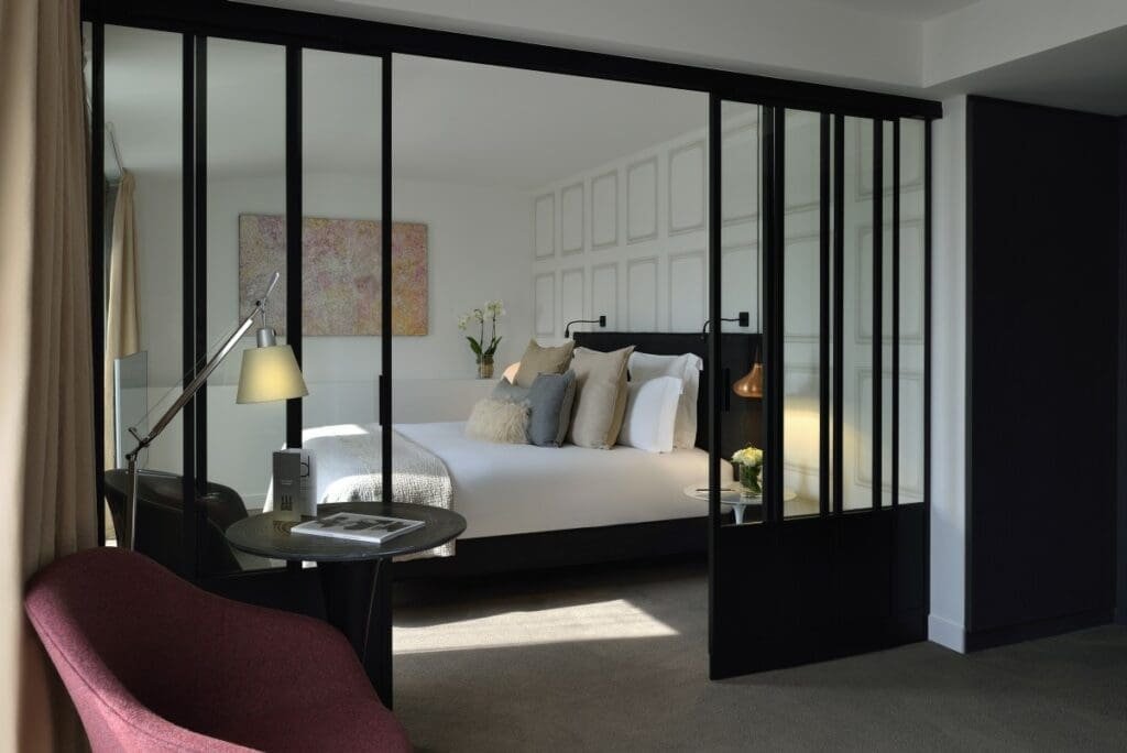 Balthazar Hotel & Spa MGallery Rennes Chambre d'hôtel Balthazar moderne avec lit blanc et cloisons vitrées noires.