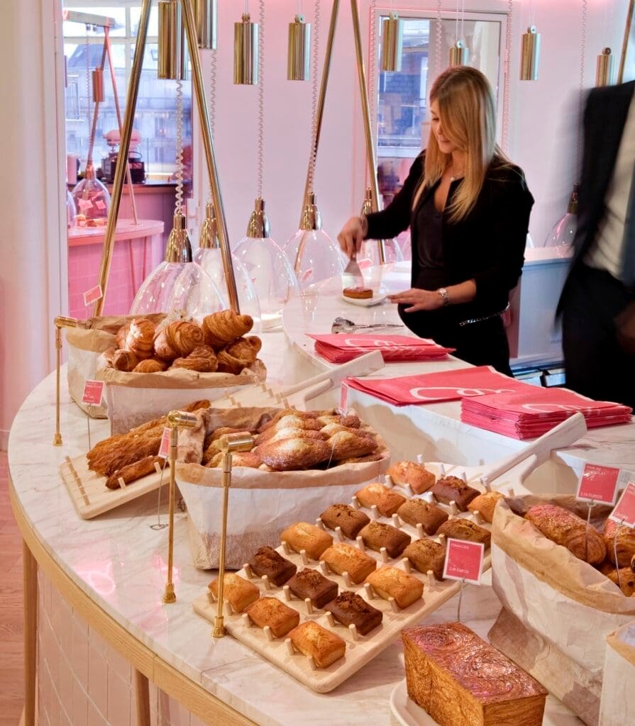 Vendedora sirviendo pasteles y bollería en una pastelería moderna.