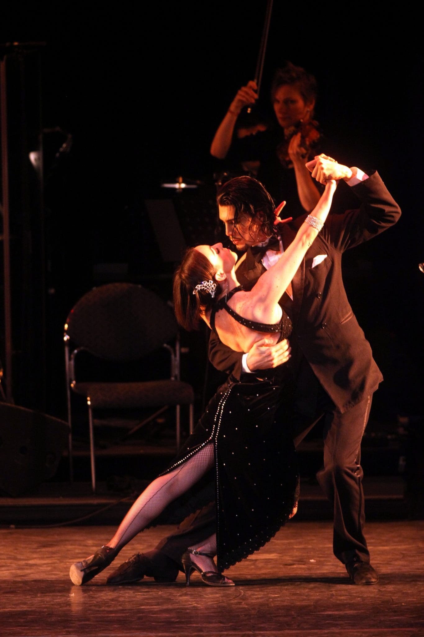Passionate tango dancer couple on stage with a violinist in the background.
