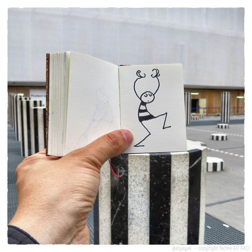 Carnet de croquis tenu, dessin de personnage rayé devant les Colonnes de Buren.