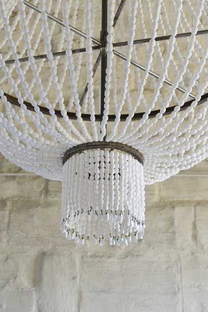 Lustre à pampilles blanches sur fond de mur en briques claires, exposition Val d’Oise.