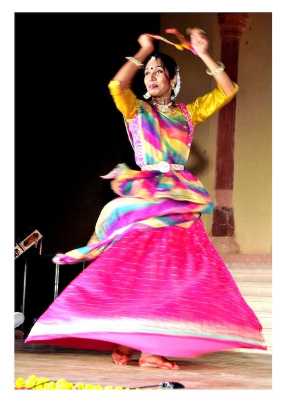 Danseuse indienne en mouvement avec jupe fuchsia et châle multicolore.
