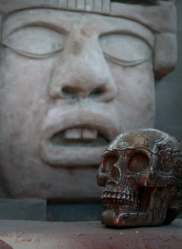 Crâne aztèque orné devant une statue maya en arrière-plan, salle La Prophétie Maya.