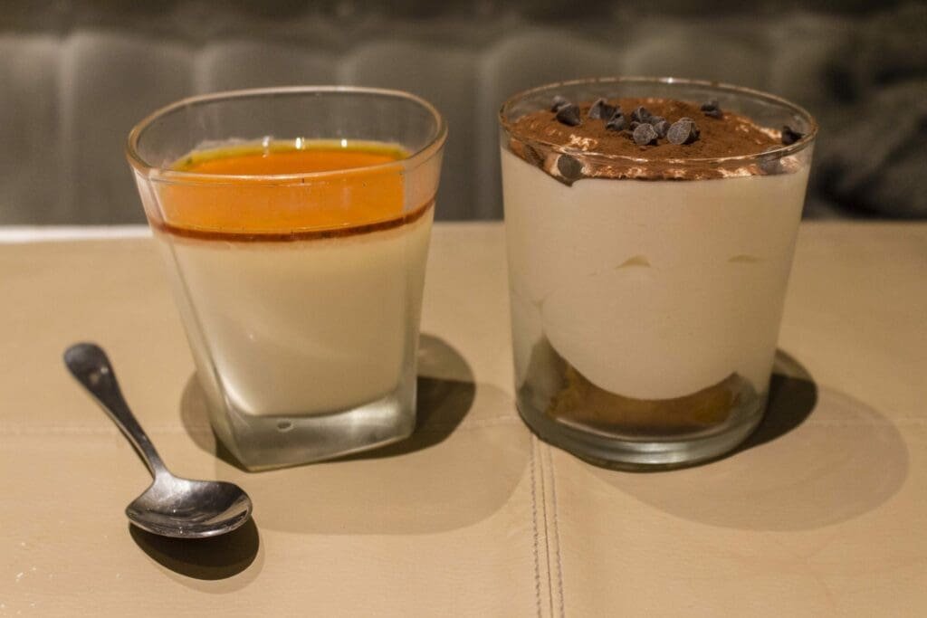 Deux desserts italiens en verrine: panna cotta et tiramisu, près d'une petite cuillère.