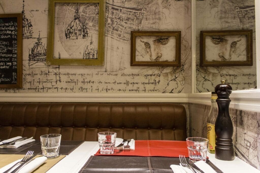Table dressée dans une pizzeria parisienne avec décor mural croquis style Léonard de Vinci.