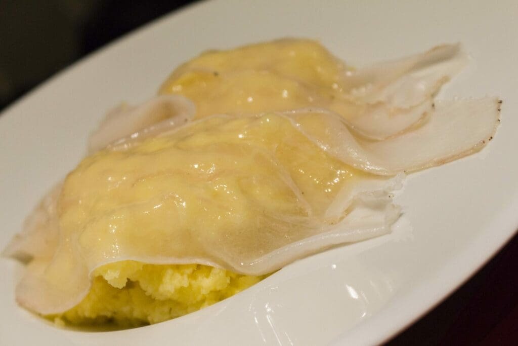 Pâtes fraîches farcies, jaunes et nappées, sur assiette blanche.