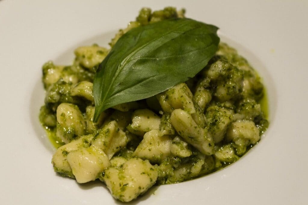 Gnocchis au pesto et feuille de basilic frais sur assiette blanche.