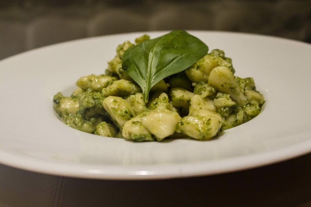 Gnocchis au pesto et feuille de basilic frais dans une assiette blanche.
