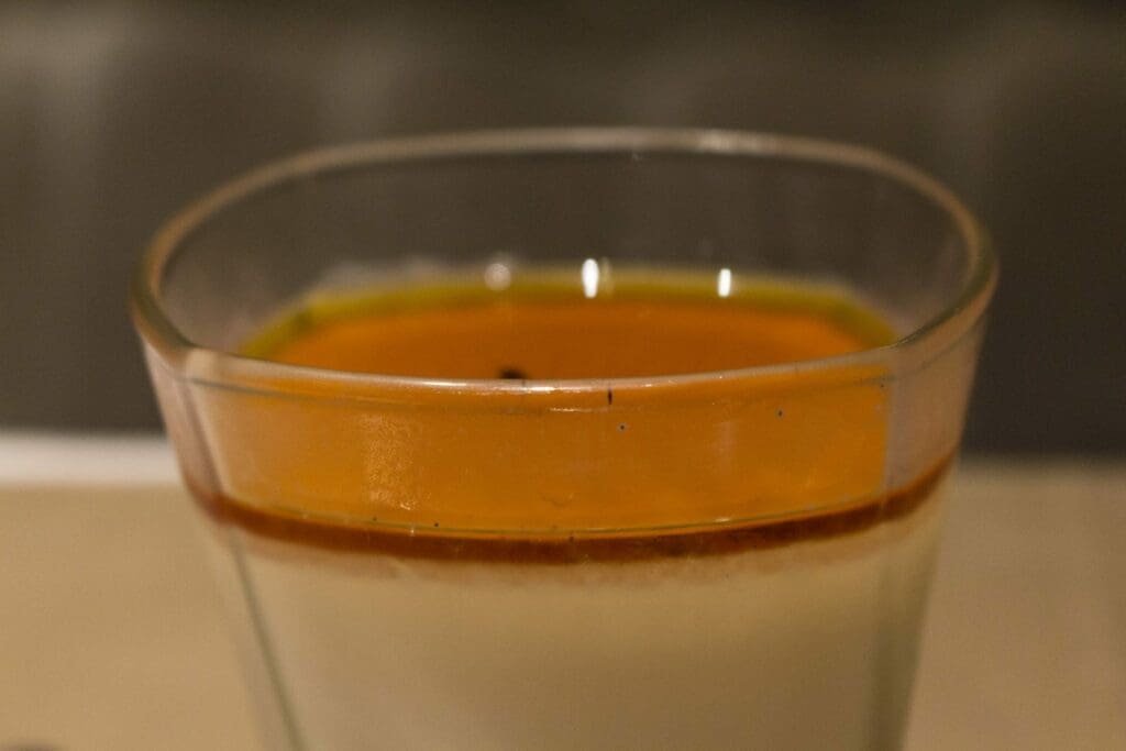 Dessert crémeux, probablement une panna cotta, dans un verre avec un coulis orange.