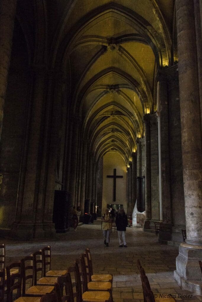 Intérieur sombre nef cathédrale Chartres avec croix et visiteurs.
