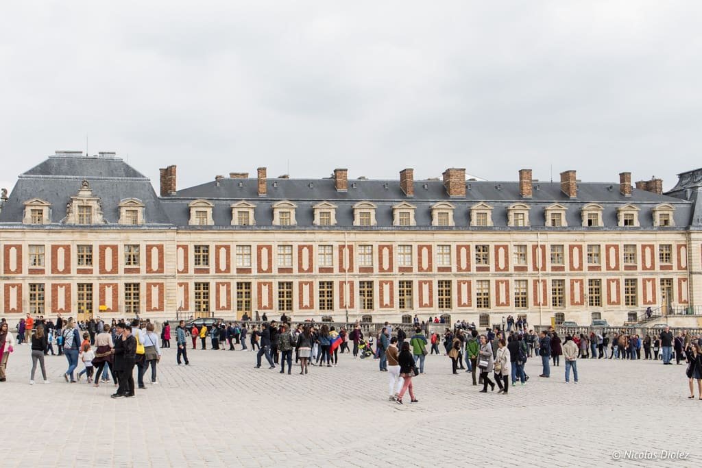 Façade du Château de Versailles avec foule sur la cour pavée.
