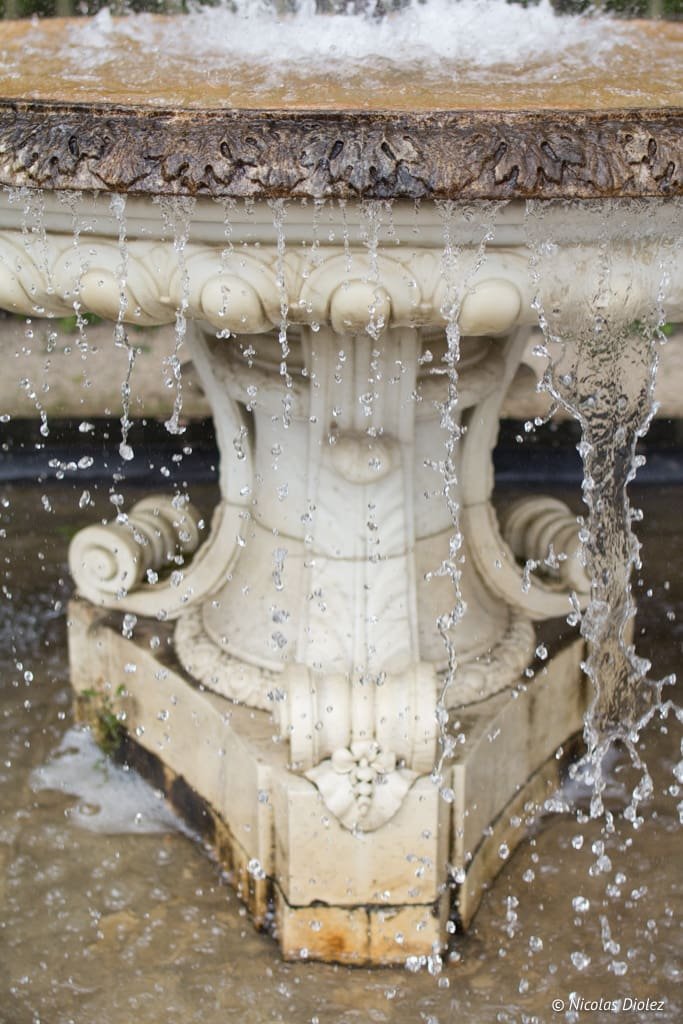 Détail d'une fontaine en marbre baroque avec de l'eau qui ruisselle et éclabousse.
