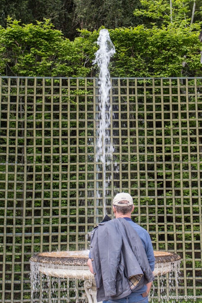 Spectateur observant une gerbe d'eau d'une fontaine dans les jardins du Château de Versailles.