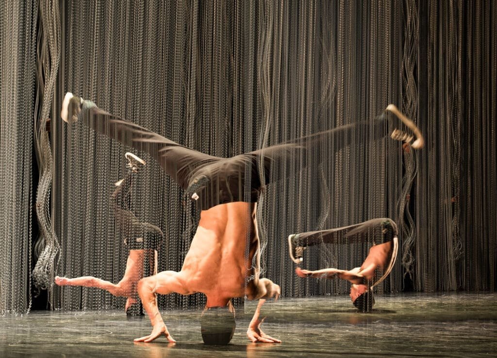 Dancer in a handstand in front of a metal chain curtain.