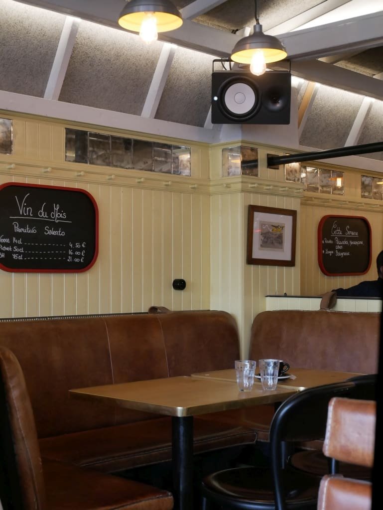 Intérieur de bistrot avec banquettes en cuir, tables et tableau "Vin du mois".