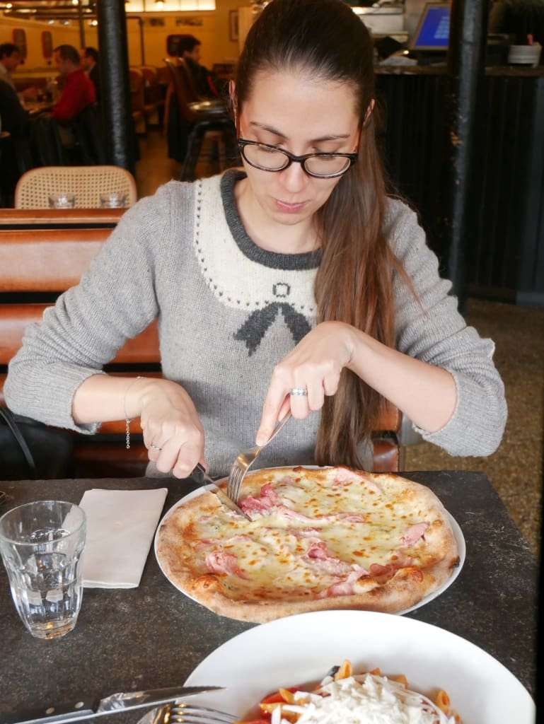 Femme coupant une pizza jambon-fromage dans une trattoria parisienne.