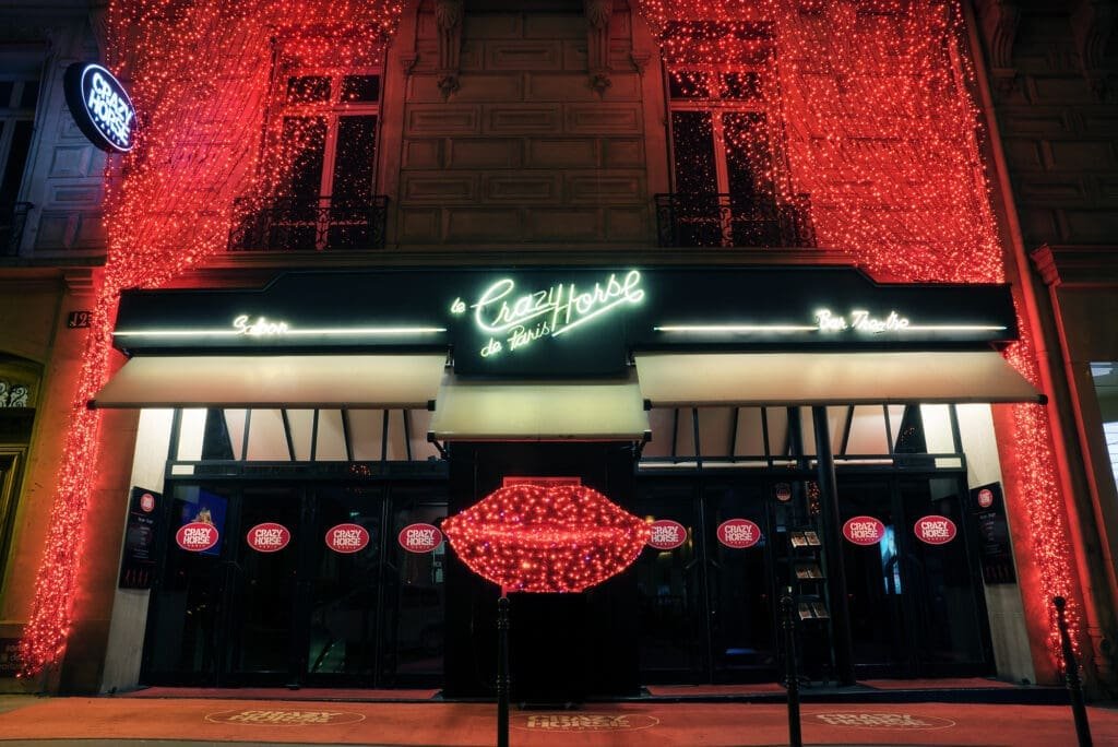 Facade CrazyHorseHD©MarkDaviesPhoto Façade du Crazy Horse de Paris la nuit, illuminée de lumières rouges et de lèvres scintillantes.
