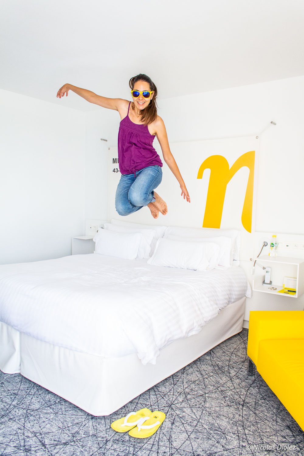 Donna sorridente che salta su un letto bianco, camera Mama Shelter Marseille.