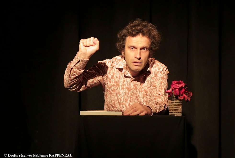 Man met krullend haar en opgeheven vuist op het podium met bloemen.