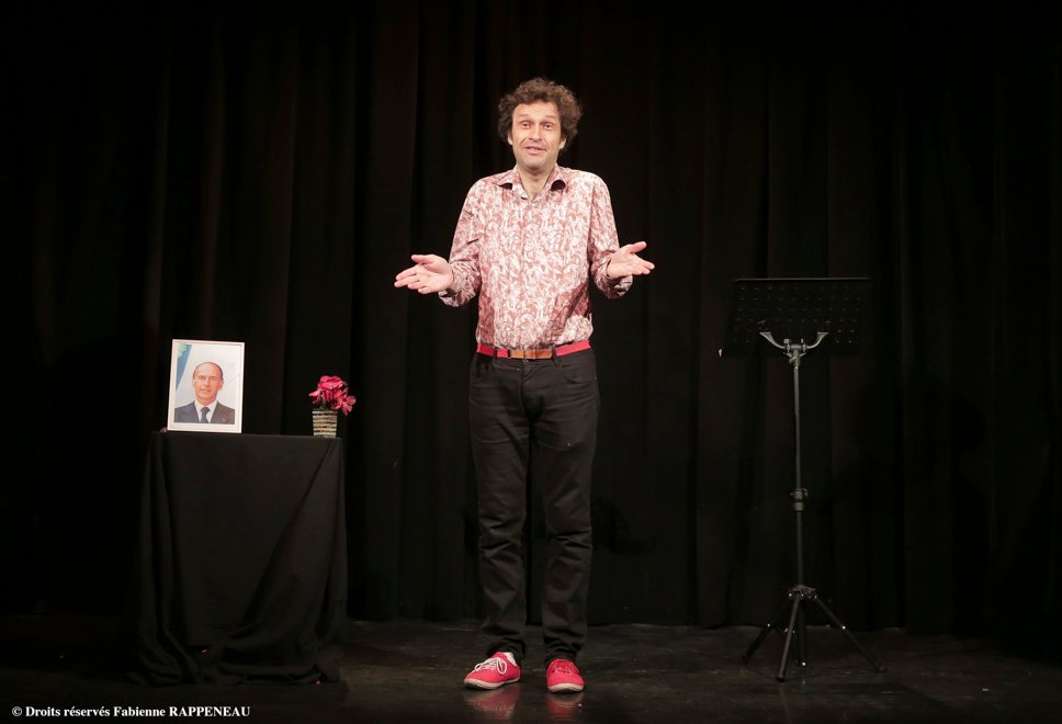 Petit Manuel D'engagement Politique Acteur op het podium met een portret van Jacques Chirac en een lessenaar.