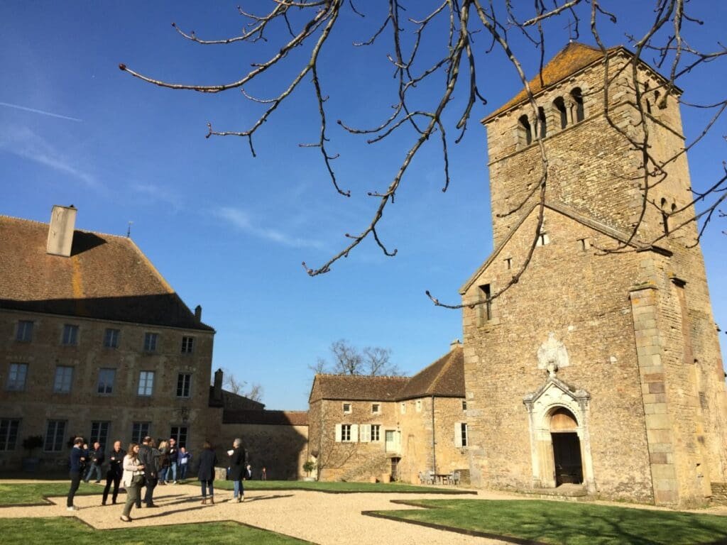 Château de Pierreclos - DR Valérie Collet 2019 Courtyard with stone tower and buildings, group visiting in front of Château de Pierreclos.